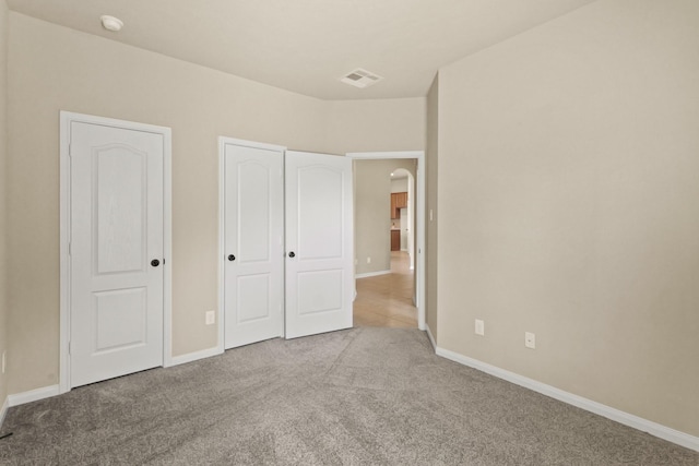 unfurnished bedroom with visible vents, arched walkways, carpet, and baseboards