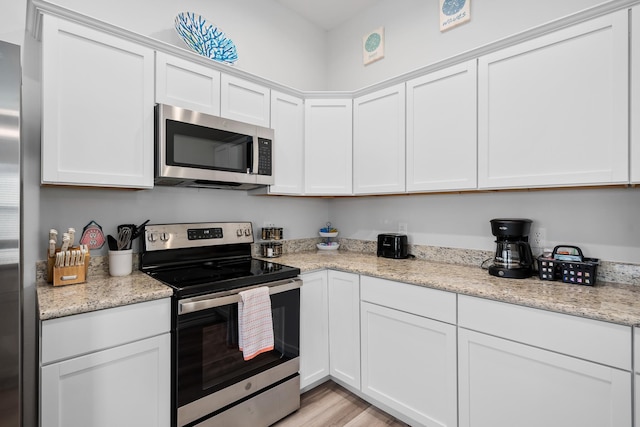 kitchen featuring white cabinets, light stone counters, light wood-style floors, and appliances with stainless steel finishes