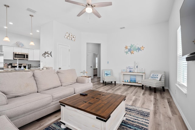living room featuring light wood finished floors, visible vents, a ceiling fan, and baseboards