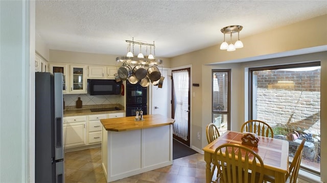 kitchen with wooden counters, black microwave, cooktop, freestanding refrigerator, and white cabinetry