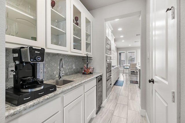 kitchen with a sink, stainless steel appliances, beverage cooler, and white cabinetry