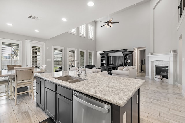 kitchen featuring visible vents, an island with sink, stainless steel dishwasher, a glass covered fireplace, and a sink