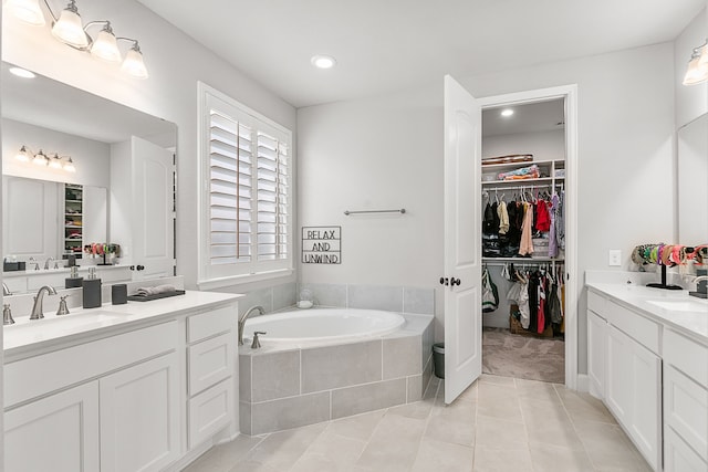 bathroom with a bath, a spacious closet, two vanities, and a sink