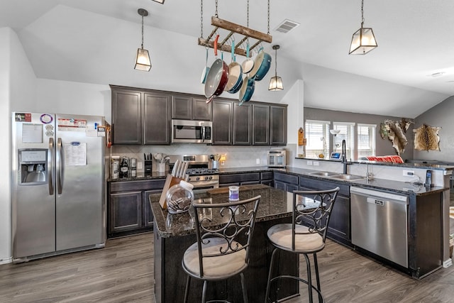 kitchen featuring dark brown cabinetry, vaulted ceiling, a peninsula, stainless steel appliances, and a sink