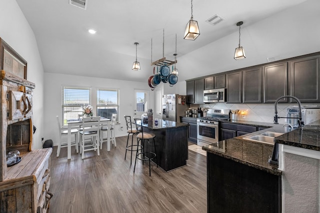 kitchen with visible vents, a breakfast bar, a sink, dark stone counters, and appliances with stainless steel finishes