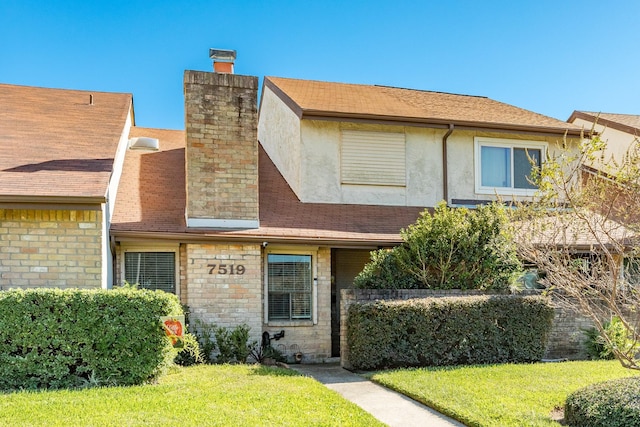 view of front of home with stucco siding, a chimney, a front lawn, and a shingled roof