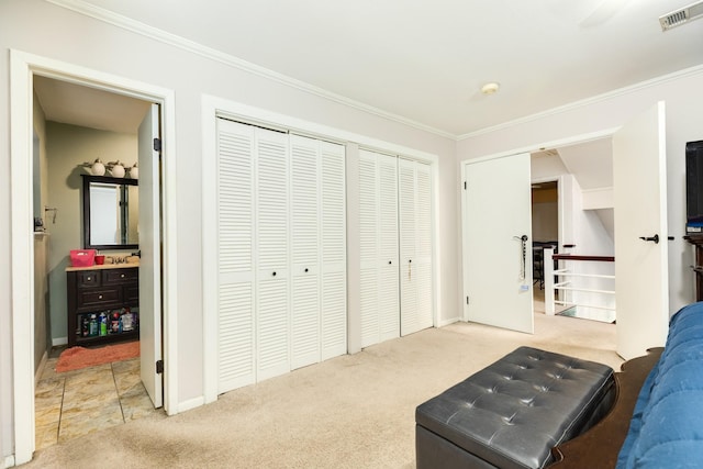 carpeted bedroom featuring visible vents, multiple closets, and crown molding