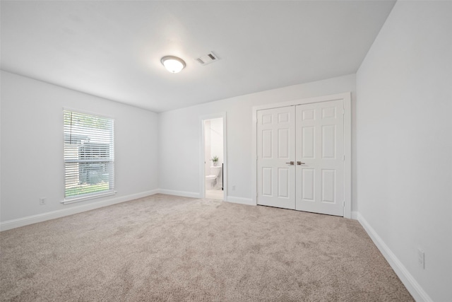 unfurnished bedroom featuring baseboards, visible vents, a closet, ensuite bathroom, and carpet flooring