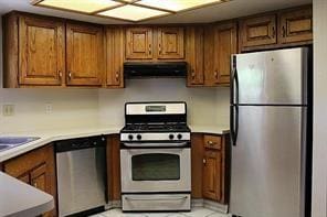 kitchen with under cabinet range hood, appliances with stainless steel finishes, brown cabinetry, and light countertops