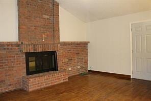 unfurnished living room with a brick fireplace, brick wall, lofted ceiling, and wood finished floors