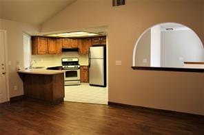 kitchen featuring dark wood finished floors, lofted ceiling, a peninsula, brown cabinetry, and stainless steel appliances