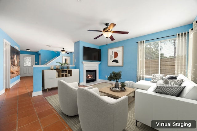 living area with a glass covered fireplace, tile patterned floors, baseboards, and ceiling fan