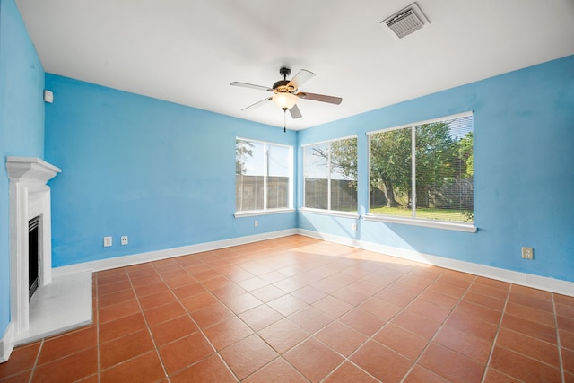 unfurnished living room featuring tile patterned floors, visible vents, a fireplace with raised hearth, baseboards, and ceiling fan