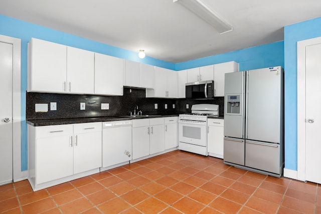 kitchen with a sink, dark countertops, tasteful backsplash, white cabinetry, and white appliances