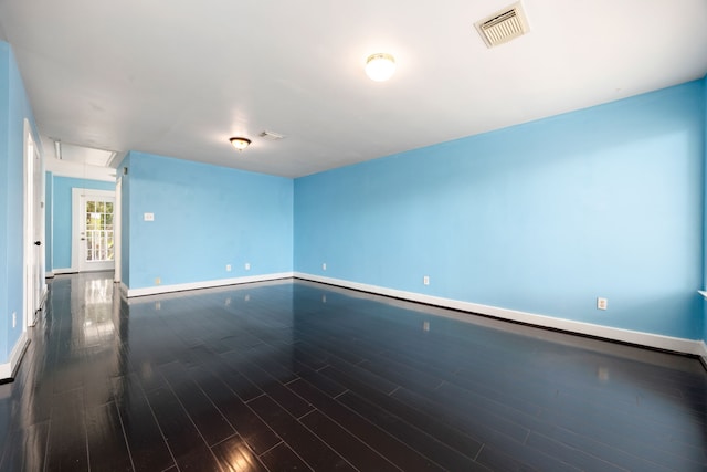 empty room with dark wood finished floors, attic access, baseboards, and visible vents