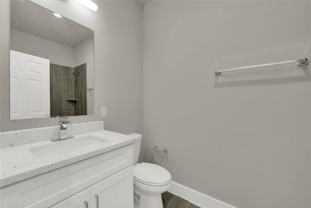 full bath with baseboards, toilet, tiled shower, wood finished floors, and vanity