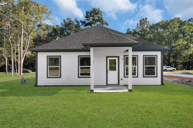 view of front of property featuring a patio, a front yard, and a shingled roof