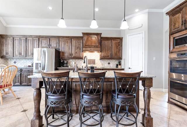 kitchen with light stone countertops, a center island with sink, appliances with stainless steel finishes, crown molding, and a kitchen breakfast bar