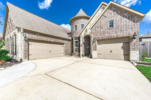 french country home featuring brick siding, an attached garage, fence, stone siding, and driveway