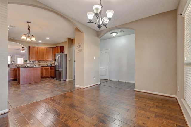 kitchen with stainless steel fridge with ice dispenser, arched walkways, brown cabinetry, baseboards, and dark wood-style floors