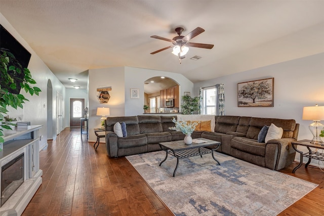 living area with baseboards, arched walkways, a ceiling fan, and dark wood-style floors