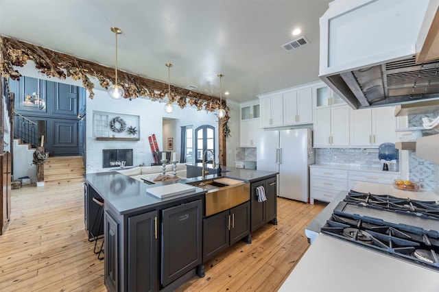 kitchen with visible vents, a fireplace, freestanding refrigerator, a sink, and white cabinetry