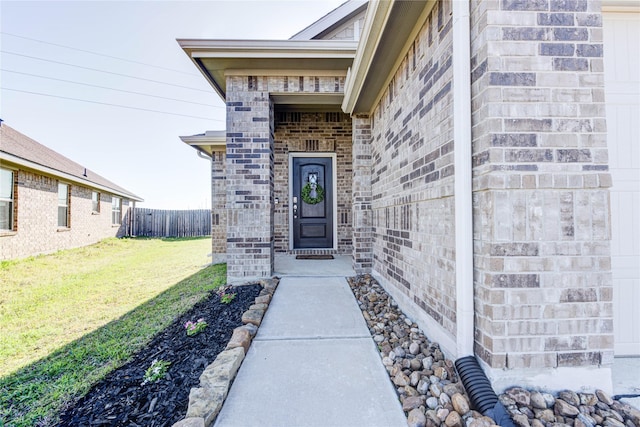 view of exterior entry featuring brick siding, a yard, and fence