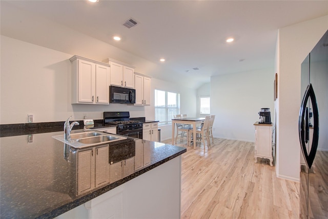 kitchen with black appliances, a sink, dark stone counters, light wood-style floors, and white cabinets