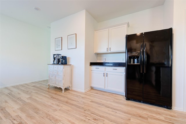 kitchen with light wood finished floors, dark countertops, baseboards, black refrigerator with ice dispenser, and white cabinets