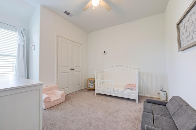 carpeted bedroom featuring a crib, visible vents, and ceiling fan