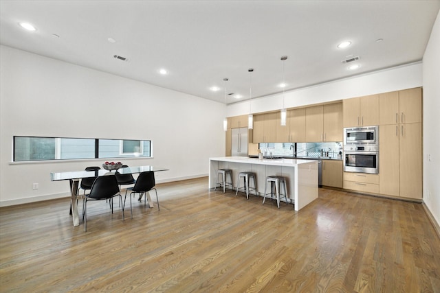 kitchen with a center island with sink, a breakfast bar area, visible vents, and built in appliances