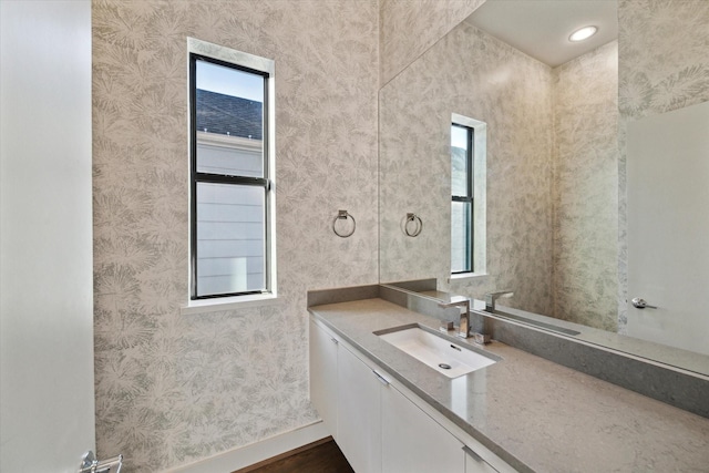 bathroom with baseboards, vanity, and wallpapered walls