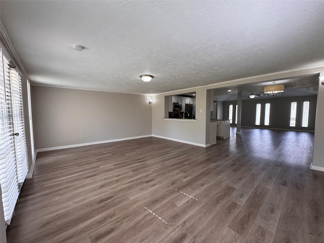 unfurnished living room featuring dark wood-type flooring, plenty of natural light, baseboards, and a textured ceiling