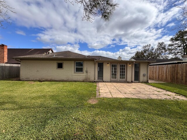 back of property featuring a fenced backyard, a lawn, brick siding, and a patio