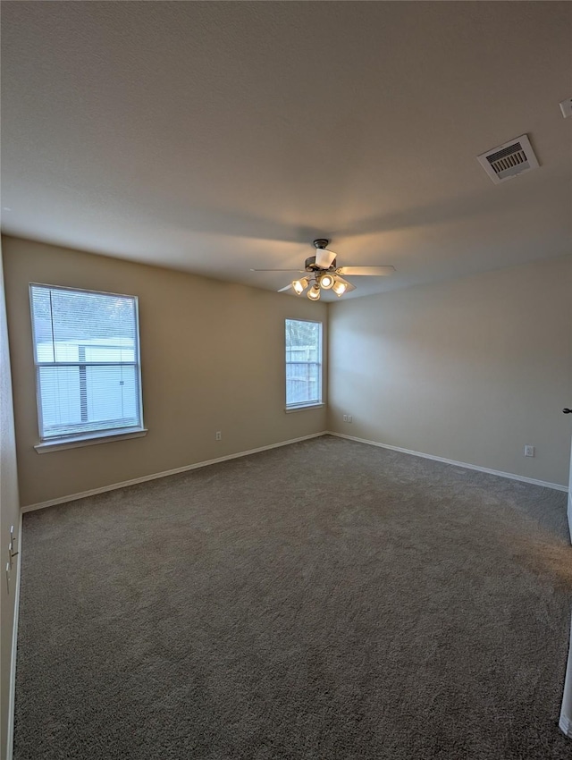 spare room with baseboards, visible vents, dark carpet, and ceiling fan