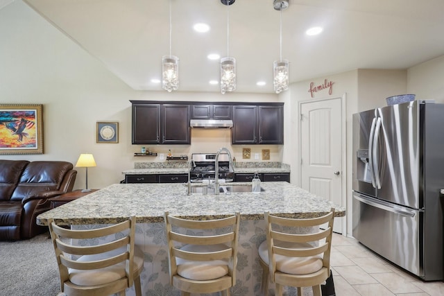 kitchen featuring a sink, stainless steel fridge, under cabinet range hood, a kitchen breakfast bar, and open floor plan