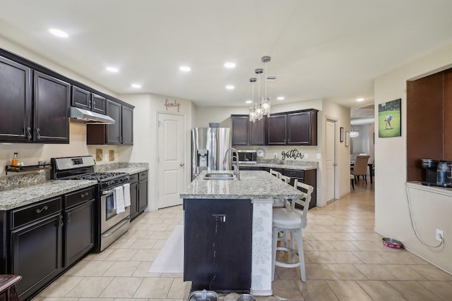 kitchen with a center island with sink, a sink, stainless steel appliances, under cabinet range hood, and a kitchen breakfast bar