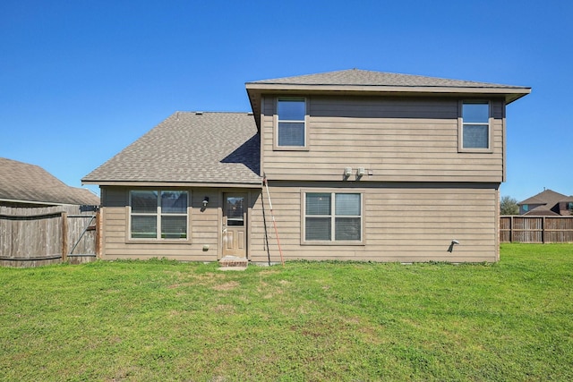 back of property with a yard, a shingled roof, and fence