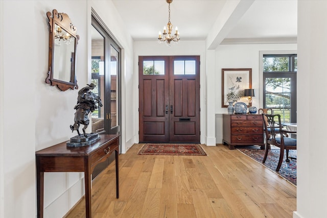 entryway with light wood finished floors, a notable chandelier, and baseboards