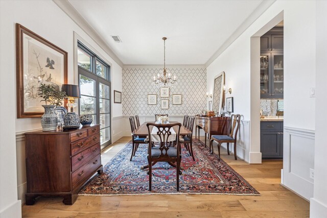 dining area featuring visible vents, wallpapered walls, a chandelier, a wainscoted wall, and light wood-type flooring