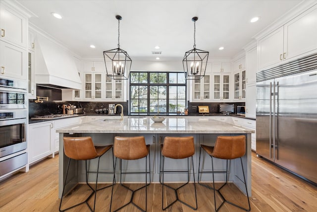 kitchen featuring light wood-type flooring, decorative backsplash, appliances with stainless steel finishes, custom exhaust hood, and white cabinetry