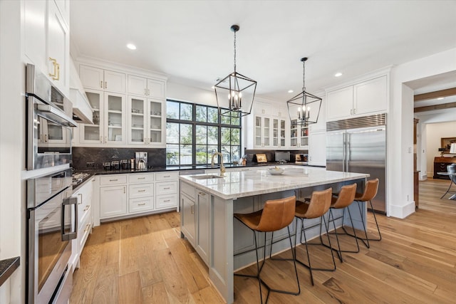 kitchen featuring an island with sink, decorative backsplash, white cabinets, stainless steel appliances, and a sink