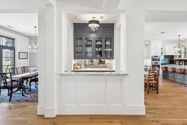 bar with a notable chandelier, light wood-type flooring, stainless steel double oven, and decorative backsplash