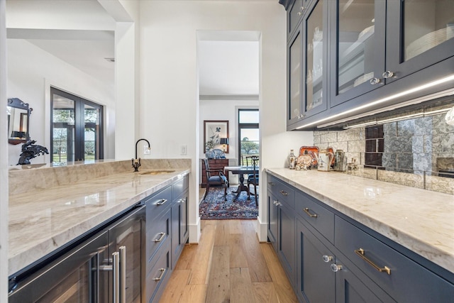 kitchen with glass insert cabinets, light stone countertops, decorative backsplash, light wood-style flooring, and a sink