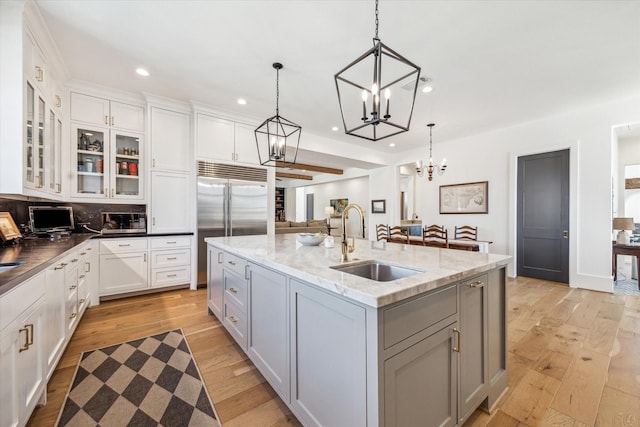 kitchen featuring a center island with sink, light wood-style flooring, a sink, white cabinets, and built in fridge