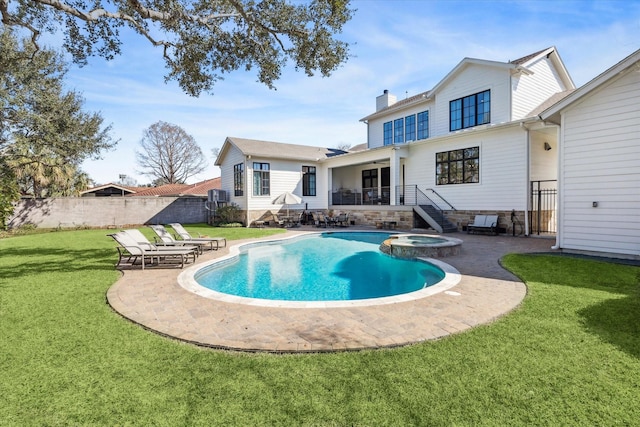 rear view of house with a pool with connected hot tub, fence, a lawn, a chimney, and a patio area