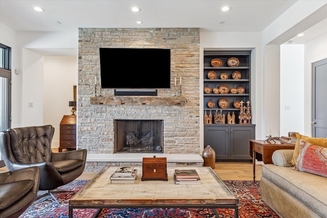 living area featuring recessed lighting, built in shelves, a stone fireplace, and wood finished floors