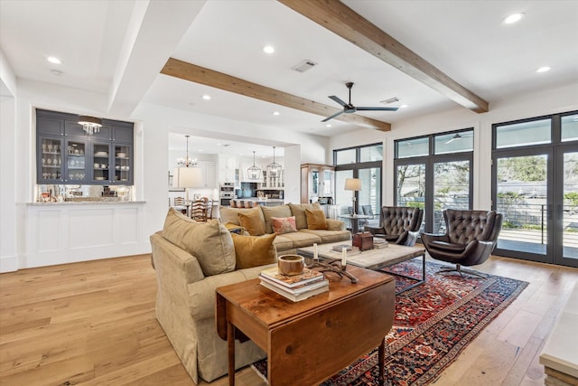 living area featuring light wood-type flooring, beam ceiling, ceiling fan with notable chandelier, recessed lighting, and french doors