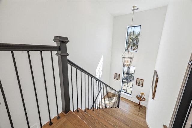 stairs featuring wood finished floors, baseboards, a towering ceiling, and a chandelier