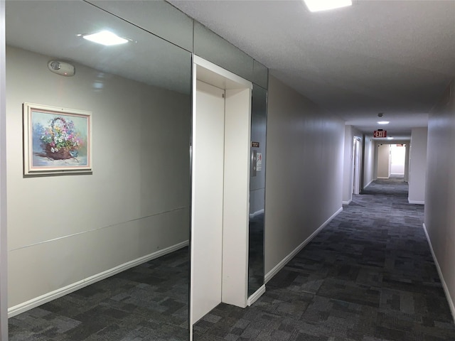 corridor featuring elevator, baseboards, and dark colored carpet